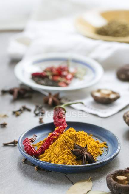 Polvo de cúrcuma, un chile seco, champiñones shiitake y anís estrellado en una mesa frente a una ventana de la cocina - foto de stock
