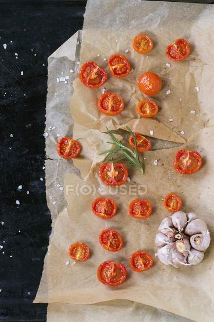 Baked cherry tomatoes with salt and garlic on backing paper — Stock Photo