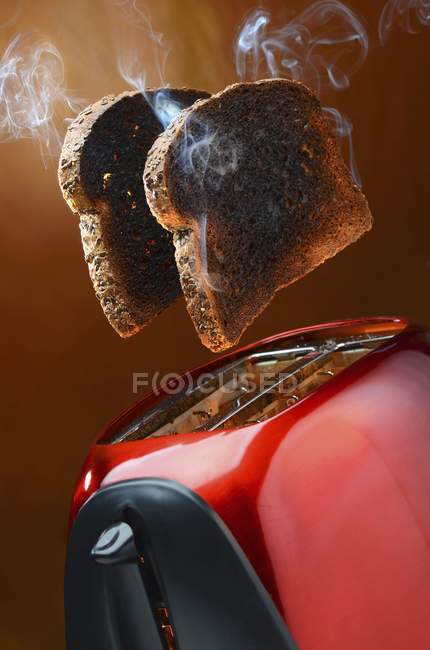 Vista de cerca de fumar tostadas integrales saltando de una tostadora roja - foto de stock