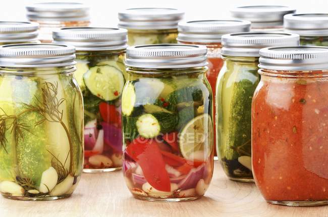 Frascos de verduras mediterráneas en conserva: pepino, calabacines, pimienta, cebolla, limón y salsa de tomate - foto de stock