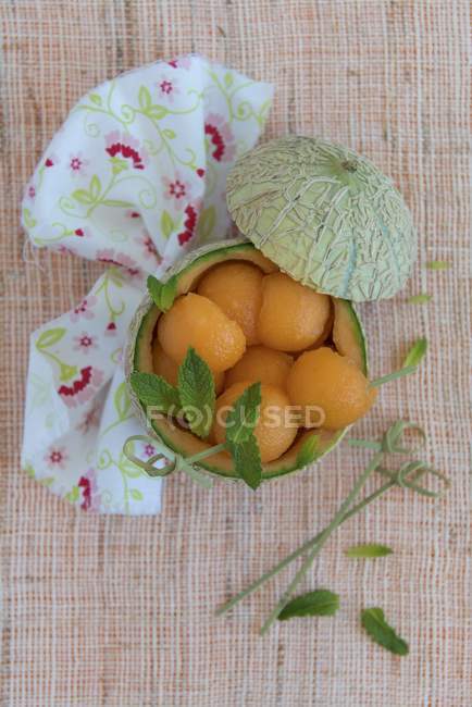 Melon balls inside scooped out melon over textile surface — Stock Photo