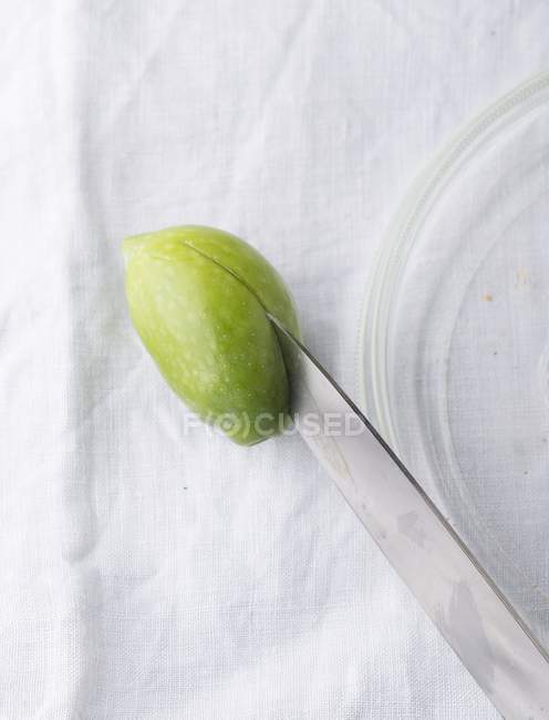Una aceituna verde que se reduce a la mitad con un cuchillo sobre la superficie textil - foto de stock