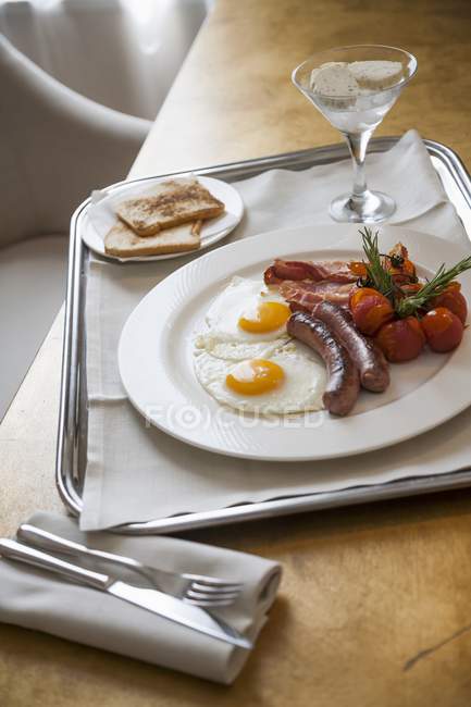 Ситний сніданок із смаженими яйцями, ковбасками, беконом та тостами — стокове фото