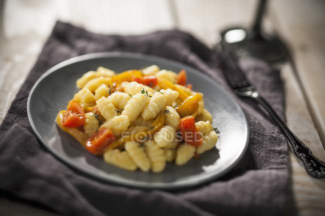 Gnocchi with peppers and tomatoes on black plate over towel — Stock Photo