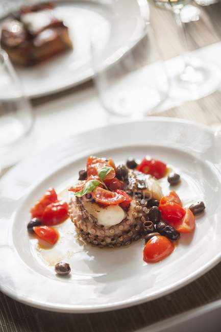 Polpo con pomodorini e olive - осьминог был помидоры черри и оливки на белой тарелке — стоковое фото
