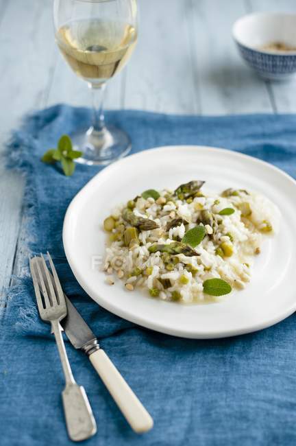 Risotto agli asparagi con piselli e salvia su piatto bianco su piatto blu con forchetta e coltello — Foto stock