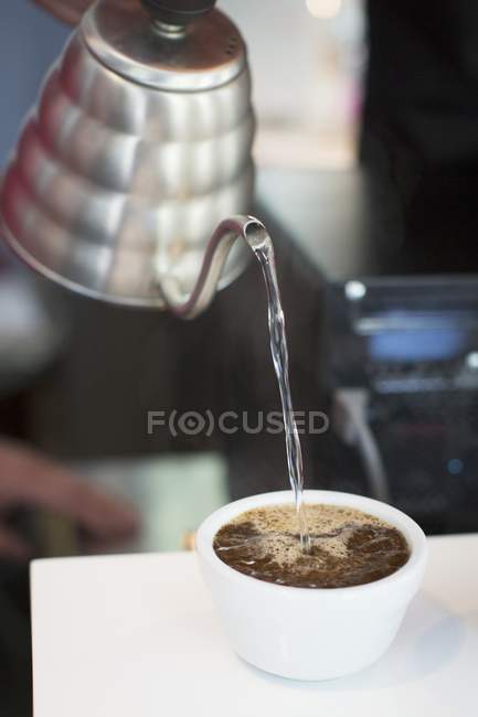 Vue rapprochée de verser de l'eau dans une tasse de grains de café — Photo de stock