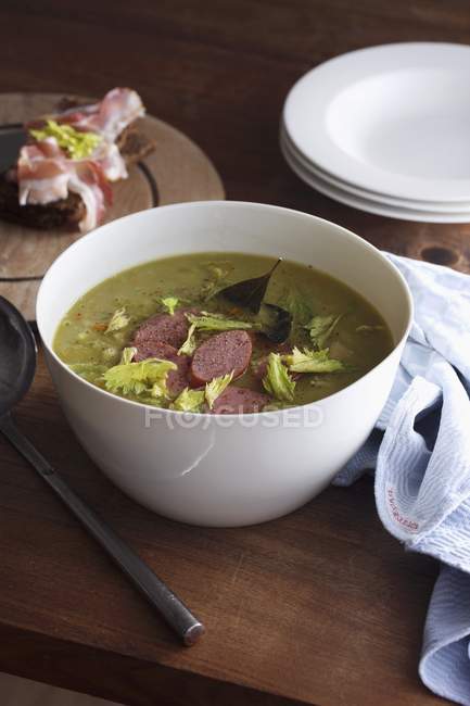 Pea soup with sausage in white bowl  over wooden surface — Stock Photo