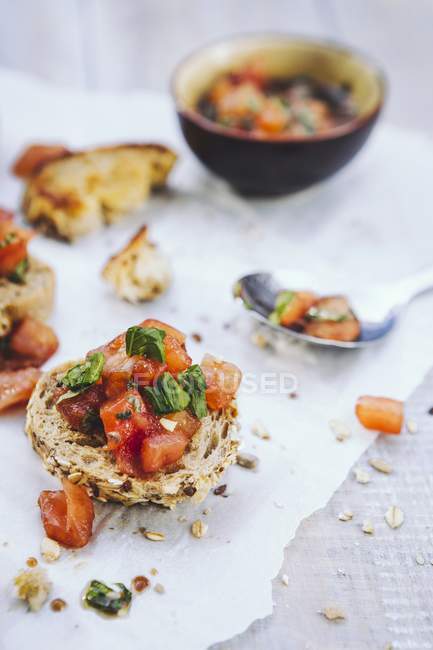 Bruschetta topped with tomatoes, basil and garlic on baking paper with spoon — Stock Photo