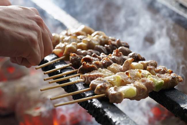 Closeup view of hand arranging Yakitori skewers on a grill — Stock Photo