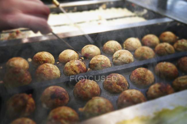 Hand arranging Takoyaki octopus balls on cooking tray — Stock Photo