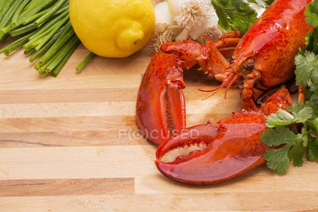 Steamed lobster with lemons and fresh vegetables  over wooden surface — Stock Photo