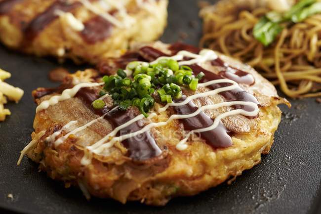 Vue rapprochée d'Okonomiyaki avec nouilles et herbes — Photo de stock