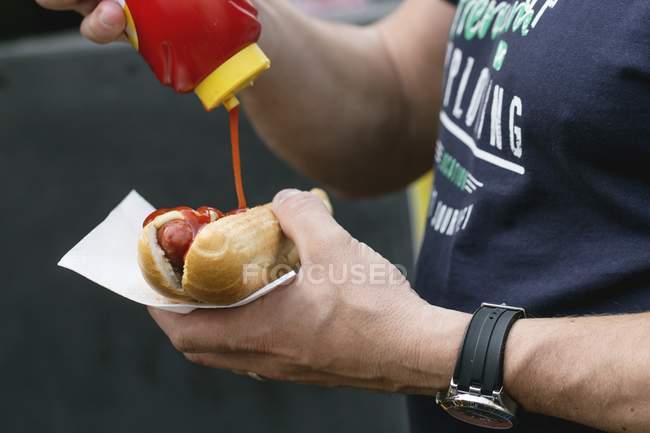 Людина наливає кетчуп на хот-дога — стокове фото