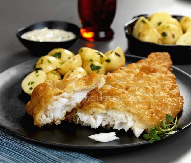 Battered plaice with herb potatoes and tartar sauce on black plate — Stock Photo