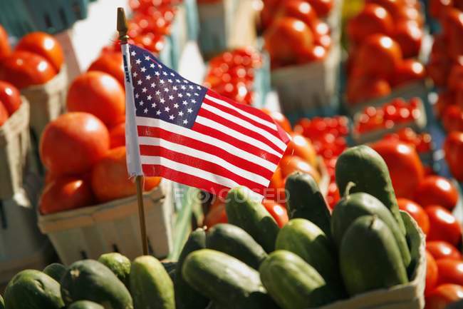 Una bandera americana entre pepinos y tomates en un mercado de agricultores - foto de stock