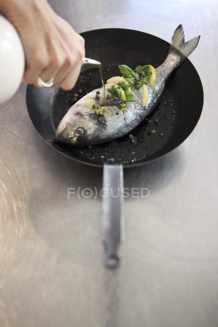 Hand drizzling fish with oil — Stock Photo