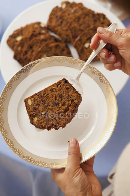 Cropped view of person holding raisin loaf slice on server over plate — Stock Photo