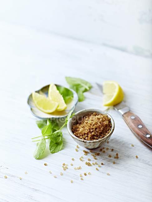 Closeup view of brown sugar with lemon wedges and mint leaves — Stock Photo
