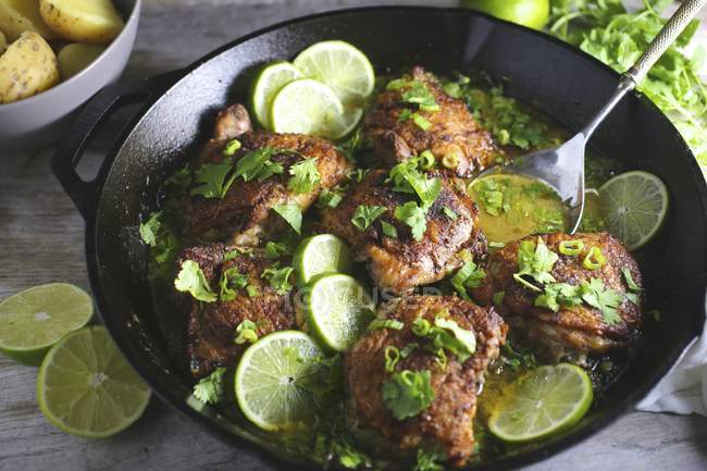 Closeup view of chicken thighs with lime slices and herbs in pan — Stock Photo