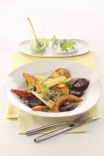 Жареные корнеплоды с травяным соусом на белой тарелке — стоковое фото