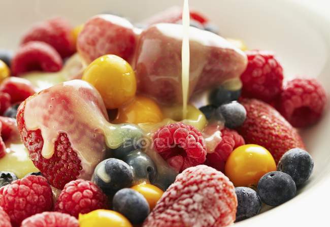 Closeup view of vanilla sauce being poured over different berries — Stock Photo