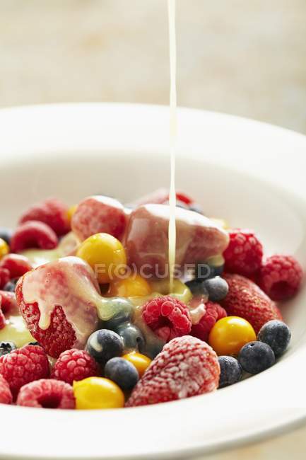 Вид крупным планом наливания ванильного соуса на ягоды в миску — стоковое фото