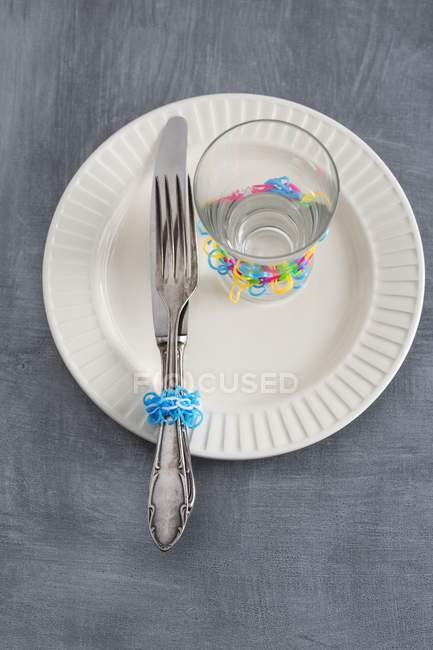 Серебряные столовые приборы и стакан, украшенный резинками на тарелке — стоковое фото