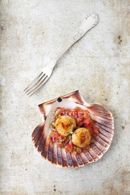 Fried scallops on tomato salsa on stone surface with fork — Stock Photo