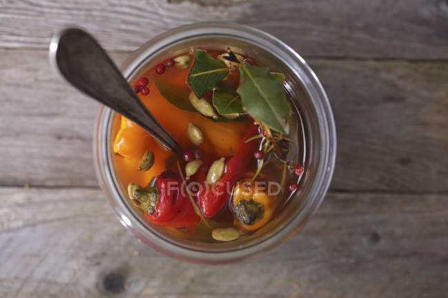 Marinated peppers in glass pot  over wooden surface — Stock Photo