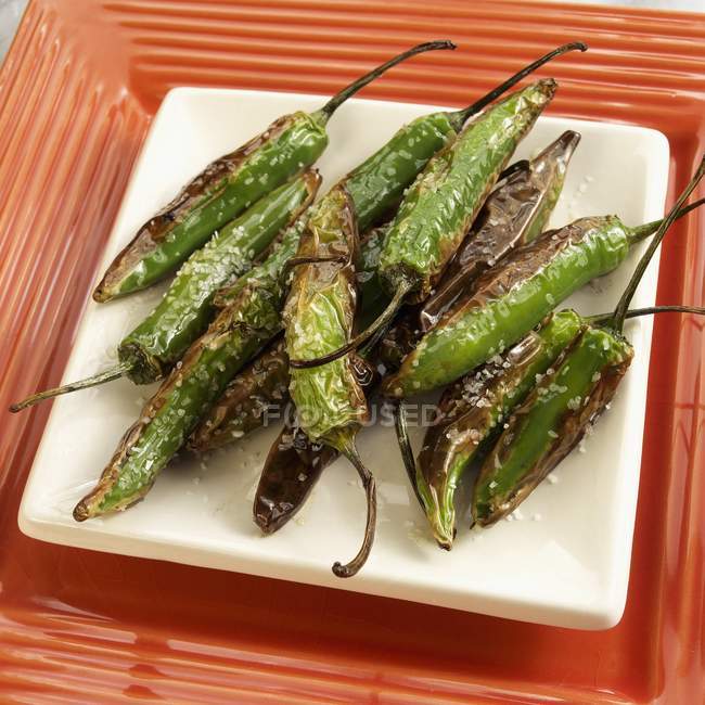 Peperoni spagnoli alla griglia su piatto bianco su piatto rosso — Foto stock