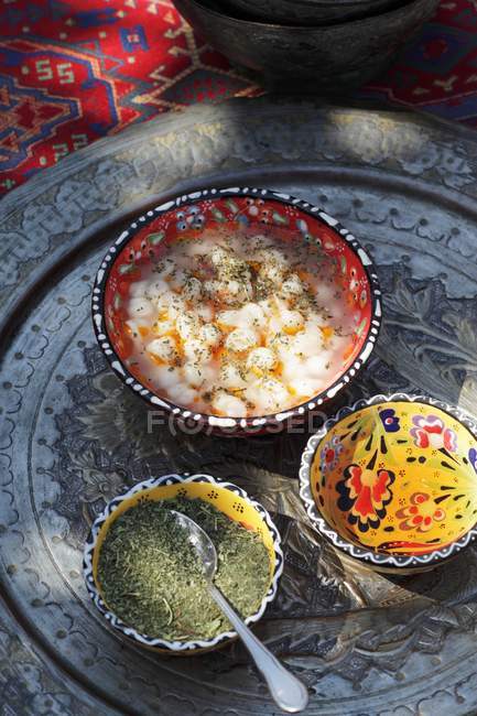 Würzige Suppe mit weißen Bohnen und Kräutern auf Teller mit Schüsseln und Löffel — Stockfoto