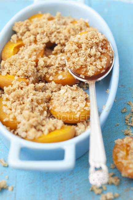 Closeup view of apricot crumble with spoon in baking dish — Stock Photo