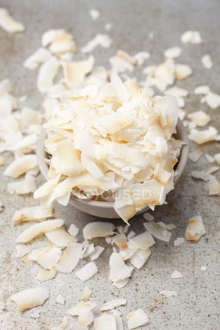 Vista close-up de flocos de coco em uma tigela cinza e espalhados ao redor — Fotografia de Stock