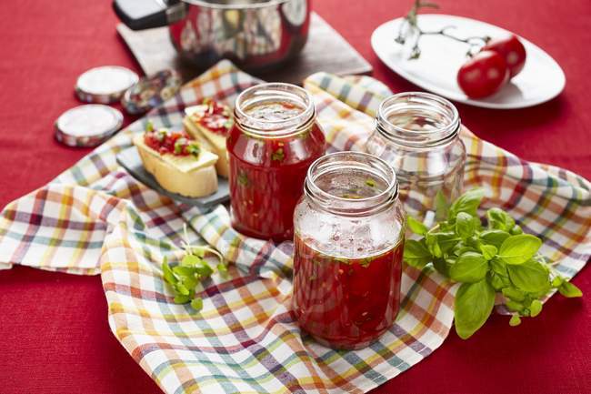 Chutney de tomates et basilic dans des bocaux en verre sur la serviette sur la table — Photo de stock