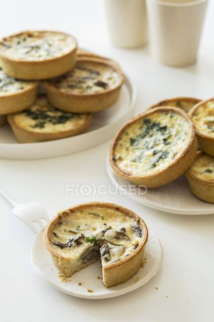 Mini spinach and mushroom quiches on white plates over table — Stock Photo