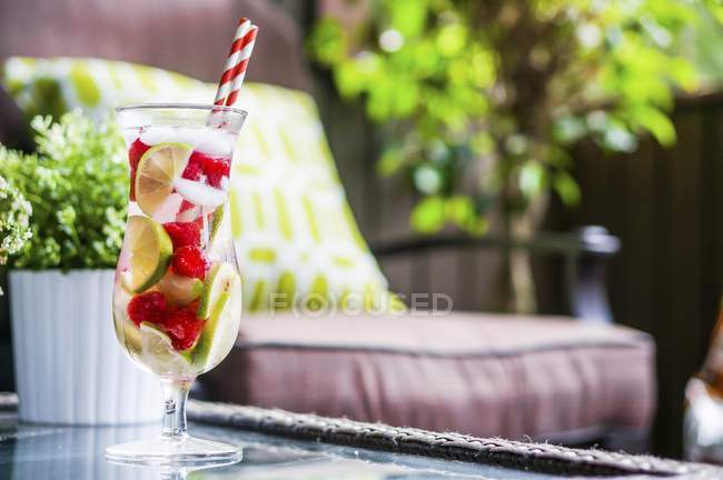 Крупный план фруктового чая со льдом в стакане для напитков с соломинками на садовом столе — стоковое фото