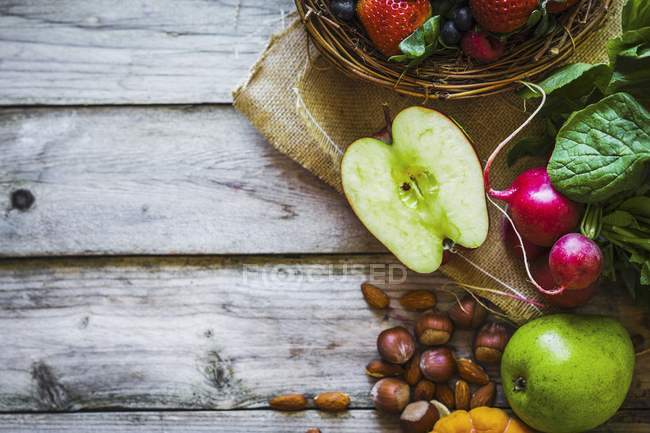 Un arreglo de frutas, verduras y nueces sobre la superficie de madera - foto de stock