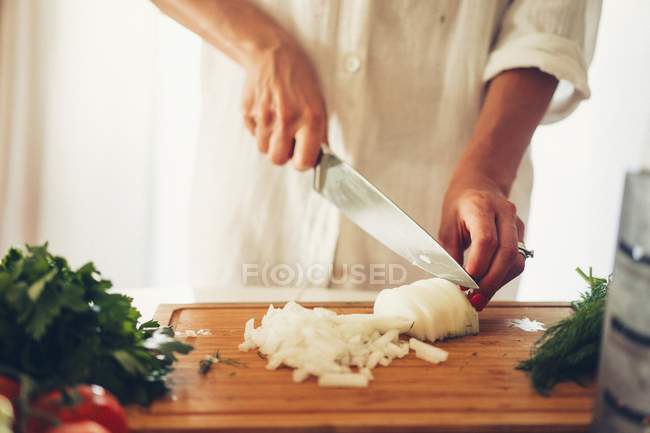 Une femme coupant un oignon dans une cuisine sur une planche à découper en bois — Photo de stock