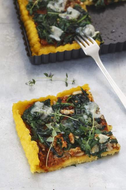 Crostata agli spinaci di polenta con pesto di pomodoro su piatto e su superficie marmorea con forchetta — Foto stock