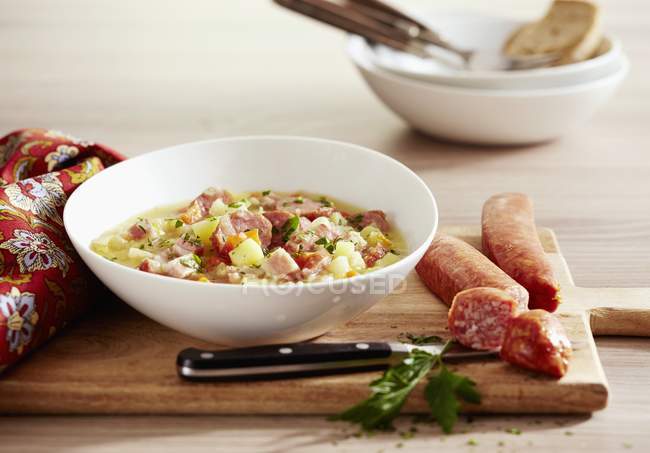 Luxembourg potato stew with bacon and sausage on white plate over wooden desk with knife — Stock Photo