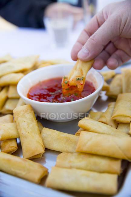 Cropped view of hand dipping fried spring roll in sauce — Stock Photo