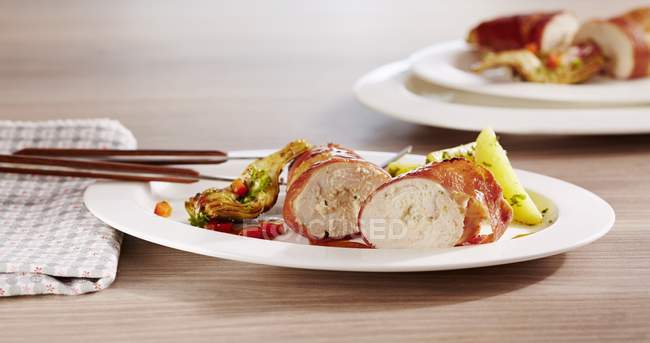 Stuffed chicken breast wrapped in ham  on white plate over wooden surface — Stock Photo