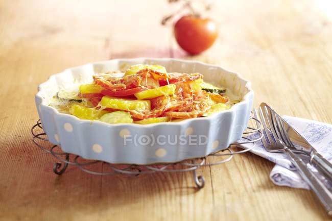 A tomato and potato gratin in white dish on stand over table — Stock Photo