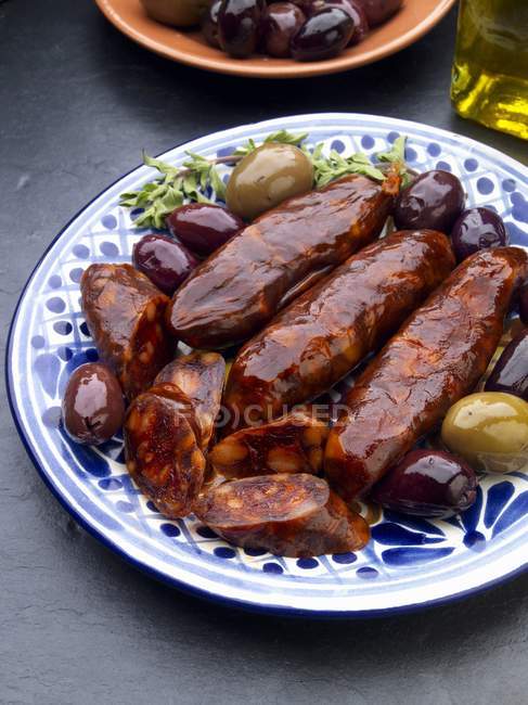 Chorizo con tapas di olive su placca bianca e blu su superficie grigia — Foto stock