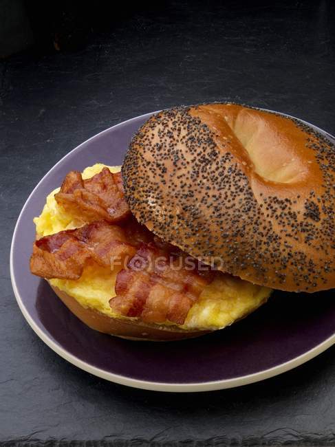Closeup view of scrambled egg and bacon on a poppy seed roll — Stock Photo