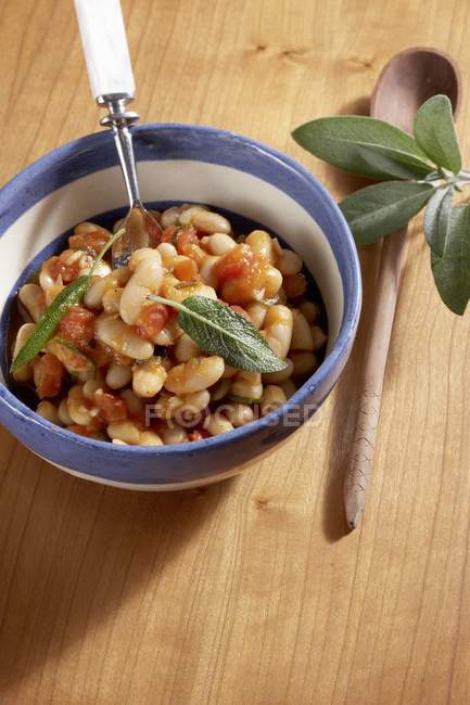Closeup view of white beans in tomato sauce with sage — Stock Photo