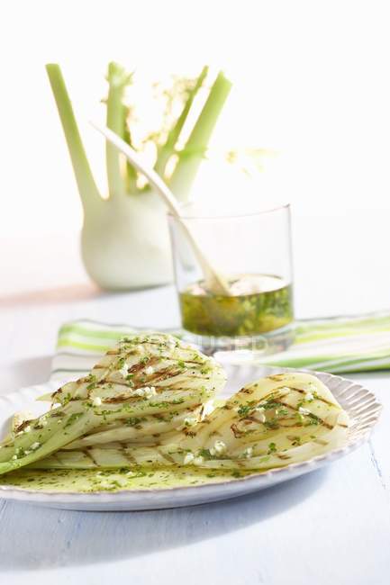 Marinated, grilled fennel with herb oil on plate over white surface — Stock Photo