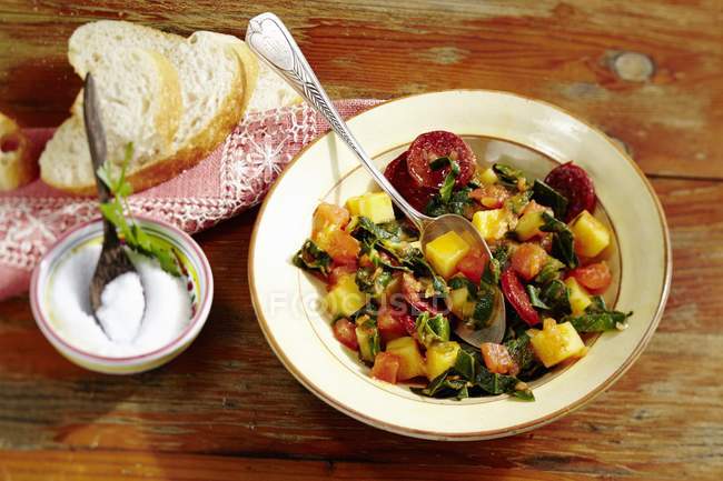 Un medley aux blettes et tomates avec chorizo sur assiette blanche avec cuillère — Photo de stock