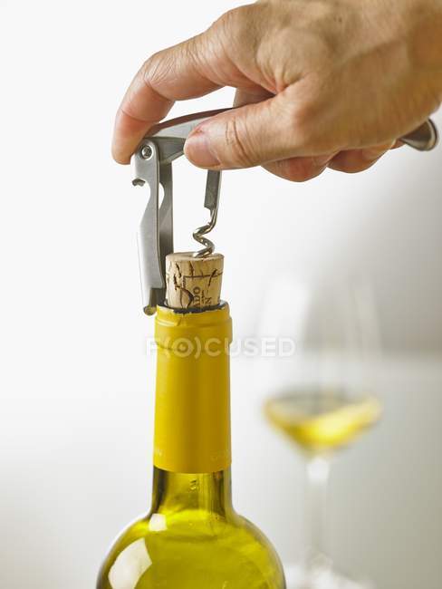 Closeup view of a hand opening a bottle of white wine with a sommelier knife — Stock Photo